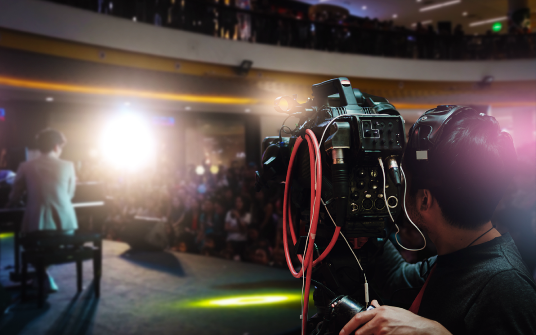 Video photographer using camcorder to record the artist plays the piano on stage in hall